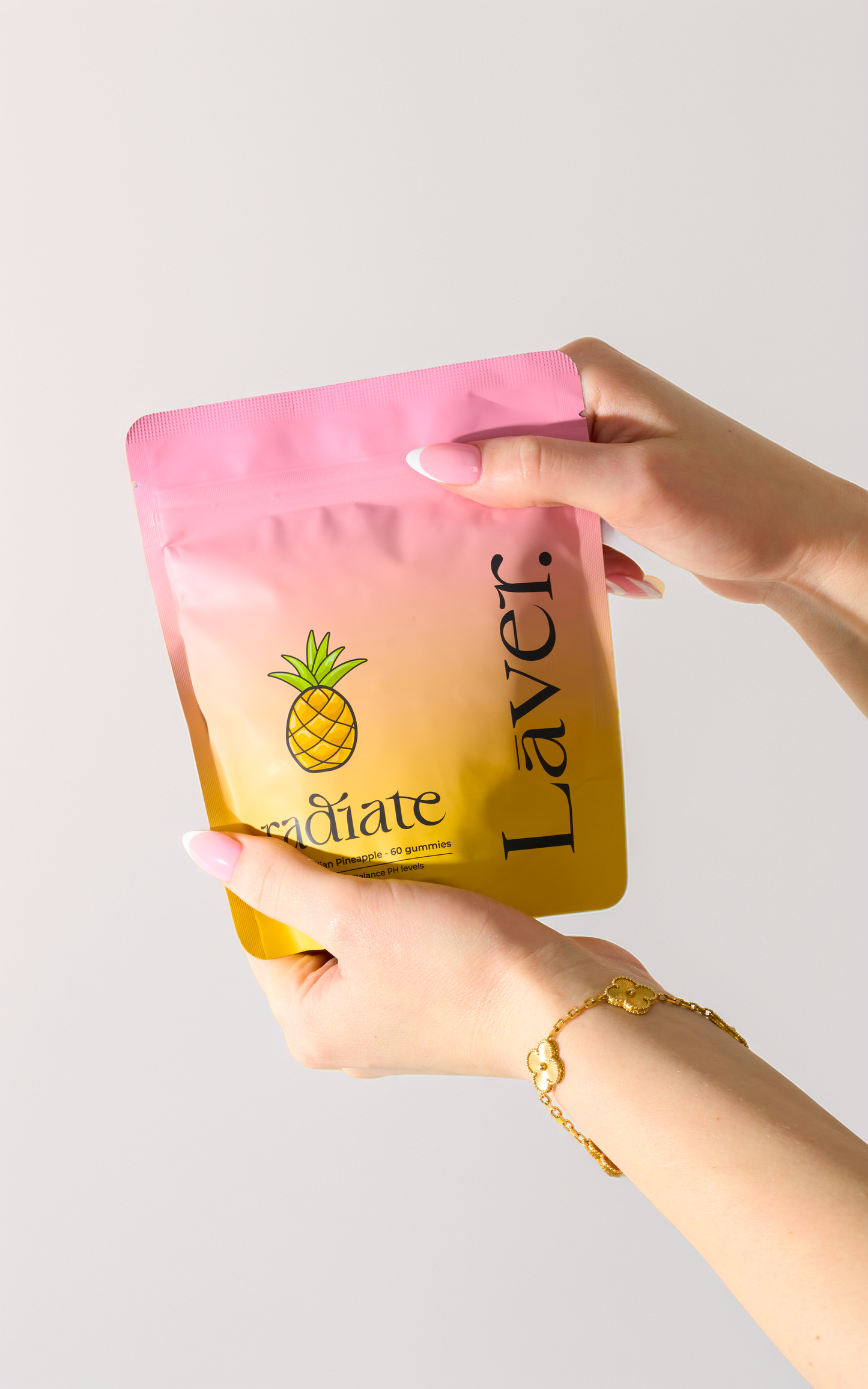 A person's hands holding a pastel pink and yellow gradient stand-up pouch with a pineapple graphic and the brand name 'Laver.' printed vertically.